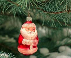 brinquedo de natal papai noel pendura em um galho coberto de neve de uma árvore de natal em um fundo festivo de neve branca bokeh com espaço de cópia. foto