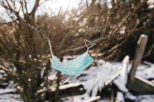 máscara azul usada em madeira, máscara facial poluição da natureza, máscaras faciais descartáveis de coronavírus descartadas, lixo nas ruas ameaça o meio ambiente, uma máscara em uma árvore em um parque foto