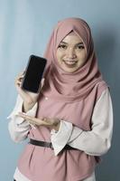 um retrato de uma jovem muçulmana asiática vestindo hijab rosa está sorrindo enquanto mostra a tela do smartphone foto