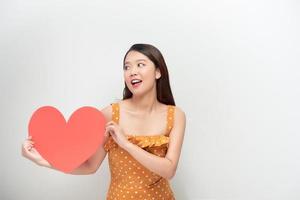 conceito de estilo de vida e férias - retrato jovem feliz no vestido de bolinhas segurando papel de coração vermelho grande. foto