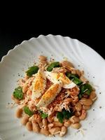 salada de peixe e feijão com um ovo em um fundo preto. foto