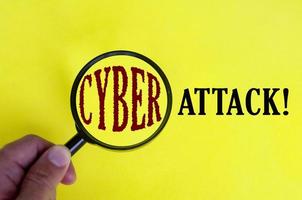 texto de ataque cibernético na capa amarela com a mão segurando a lupa. conceito de segurança na internet foto