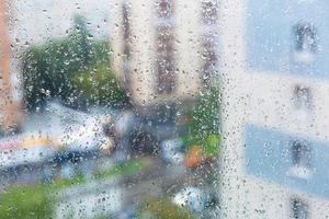 gotas de chuva no vidro da janela e rua da cidade turva foto