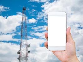 mão segure smartphone móvel com torre de telecomunicações foto