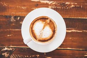 arte com leite em forma de coração em xícara de café branco na mesa de madeira no café restaurante foto