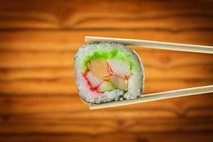 rolo de sushi com pauzinhos sobre fundo de madeira foto