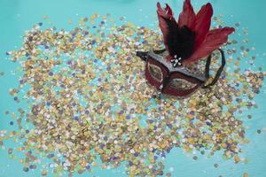 confete espalhado sobre fundo azul com uma máscara de carnaval feminina foto