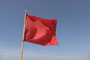bandeira vermelha balançando ao vento em um fundo de céu azul foto