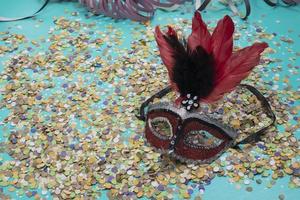 confete espalhado sobre fundo azul com uma máscara de carnaval feminina foto