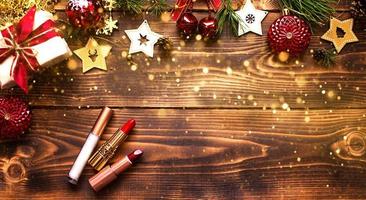 batom vermelho e brilho labial e pálpebras em um fundo de madeira na decoração de natal. maquiagem de férias para o ano novo, presente, compras, desejos femininos. espaço para texto, configuração plana foto