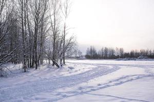 paisagem de inverno - neve branca com vestígios de sapatos e esquis no campo. a pista de esqui e a estrada contornando a floresta com árvores nuas, sol suave. foto