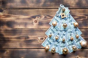 árvore de natal feita de notas de 100 dólares em fundo de madeira com copyspace e chave de casa. decoração de natal de finanças, poupança, riqueza, despesas no ano novo. imobiliário, habitação, hipoteca, realocação foto