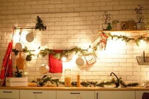 decoração de natal na cozinha, preparando-se para a celebração. luzes de guirlandas, pratos, lâmpadas incandescentes em estilo loft. árvore de natal, utensílios de cozinha. véspera de ano novo, natal. interior da casa foto