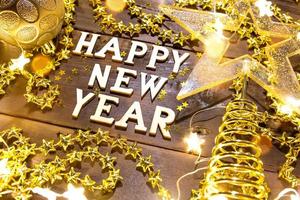 feliz ano novo letras de madeira em um fundo festivo com lantejoulas, estrelas, luzes de guirlandas. saudações, cartão postal.