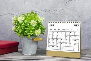 calendário de mesa de maio de 2023 na mesa de madeira com vasos de plantas e livros. foto