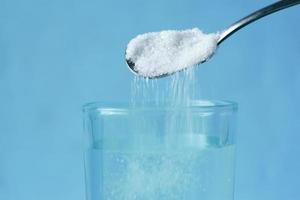 derramando açúcar branco em um copo de água na mesa