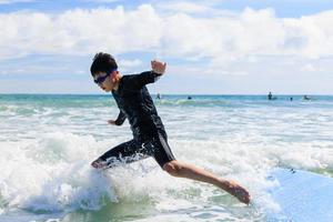 jovem rapaz, um novo aluno de surf, perde o controle e cai de uma prancha de surf na água durante a aula. foto