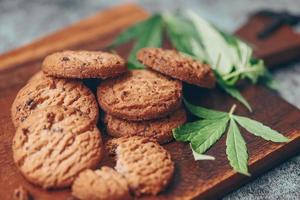 biscoitos de comida de cannabis com erva de maconha de folha de cannabis em fundo de madeira, biscoito de sobremesa doce delicioso com planta de folha de cânhamo thc cbd ervas lanche de comida e conceito médico foto