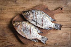 dois peixes de água doce de tilápia do nilo cru na placa de madeira de madeira - peixe tilápia fresco para cozinhar alimentos foto