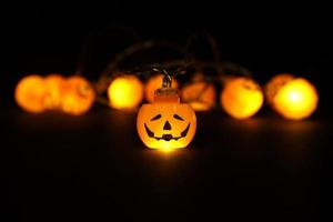 luzes de guirlanda de abóboras laranja brilhantes de halloween com espaço de cópia acima e abaixo em fundo preto. luzes desfocadas de bokeh, um rosto de abóbora focado, close-up. feriado festivo conceito de halloween. foto