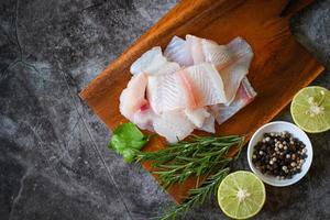 filé de peixe na placa de madeira com ingredientes para cozinhar, filé de peixe pangasius cru fresco com ervas e especiarias pimenta preta limão limão e alecrim, carne dolly peixe tilápia listrado peixe-gato foto