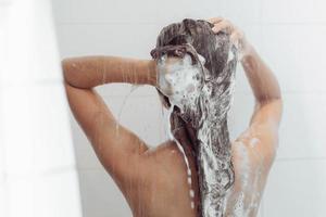 jovem mulher lavando o cabelo no chuveiro. mulher asiática lavando o cabelo preto. foto