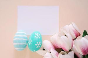 conceito de feliz páscoa com cartão em branco, ovos de páscoa coloridos e tulipas cor de rosa. vista superior com espaço de cópia foto