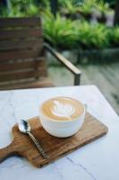 xícara quente de café latte art serve na bandeja de madeira com colher no jardim foto