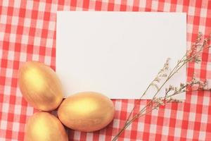 ovos de páscoa dourados sobre fundo de toalha de mesa quadriculada vermelha com cartão blang, feliz feriado de páscoa foto