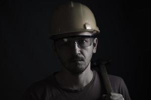 cara de mineiro em background.head preto cansado mineiro no capacete e óculos. ele tem um martelo nos ombros. foto