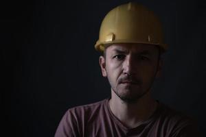 mineiro sujo no capacete amarelo em fundo escuro. retrato do rosto de perto. foto