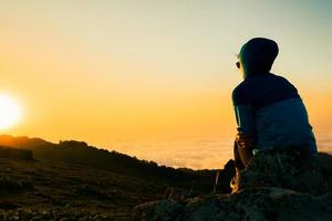 solitária mulher feliz retrato assistir nascer do sol. mulher de turista despreocupada olhando o sol apreciando a paisagem. viajante de garota no topo da montanha em raios do pôr do sol. alpinista está curtindo a natureza foto