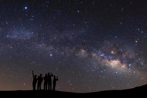 paisagem com Via Láctea, céu noturno com estrelas e silhueta de um homem desportivo em pé com os braços levantados na montanha alta. foto