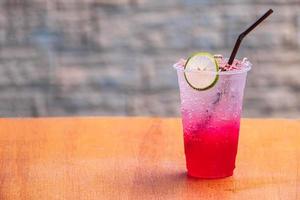 o suco vermelho, refrigerante vermelho água-limão refrigerante com limão slide na mesa de madeira e fundo desfocado foto