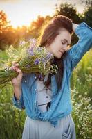 linda garota andando no campo no verão com flores silvestres. foto