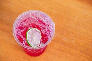 o suco vermelho, refrigerante vermelho água-limão refrigerante com limão slide na mesa de madeira e fundo desfocado foto