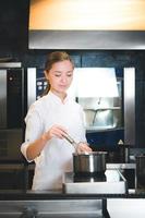 retrato de chef jovem confiante e sorridente vestido de uniforme branco, cozinha profissional estão em segundo plano foto