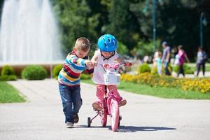 menino e menina no parque aprendendo a andar de bicicleta foto