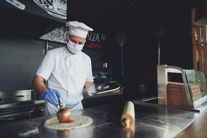 chef com máscara facial protetora de coronavírus preparando pizza foto