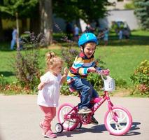 menino e menina no parque aprendendo a andar de bicicleta foto