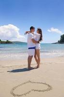 casal feliz se diverte na praia com coração na areia foto