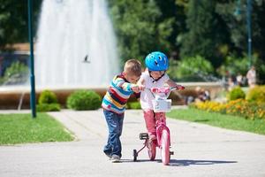 menino e menina no parque aprendendo a andar de bicicleta foto