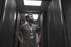 retrato de técnico masculino ou administrador de rede em pé corajoso como um herói com os braços cruzados na sala do servidor do data center. foto