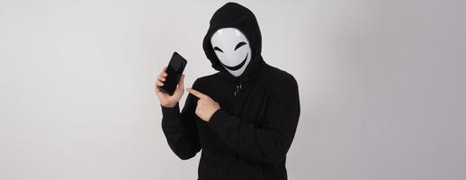 hacker anônimo e máscara facial com smartphone na mão. foto