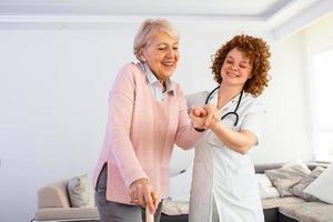 enfermeira sorridente, ajudando a senhora idosa a andar pelo lar de idosos. retrato de cuidadora feliz e mulher sênior caminhando juntos em casa. cuidador profissional cuidando de mulher idosa. foto