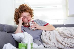 mulher deprimida deitada em uma mesa com uma xícara de café na mão, jovem deprimida chateada deitada no sofá sentindo dor de cabeça enxaqueca, adolescente sonolento triste cansado menina exausta está nervoso e estressado foto