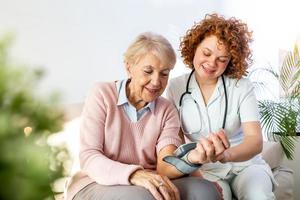 cuidador medindo a pressão arterial da mulher idosa em casa. cuidador gentil medindo a pressão arterial de uma mulher idosa feliz na cama no lar de idosos. foto