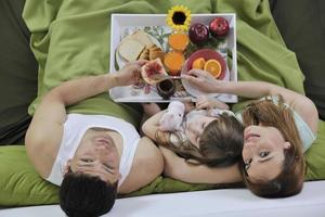 família jovem feliz toma café da manhã na cama foto