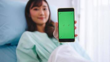 feliz jovem paciente do sexo feminino asiático mostrando smartphone com tela verde durante a hospitalização. foto