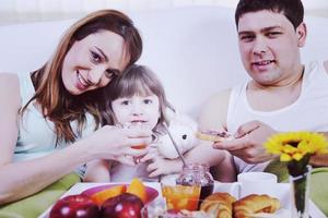 família jovem feliz toma café da manhã na cama foto